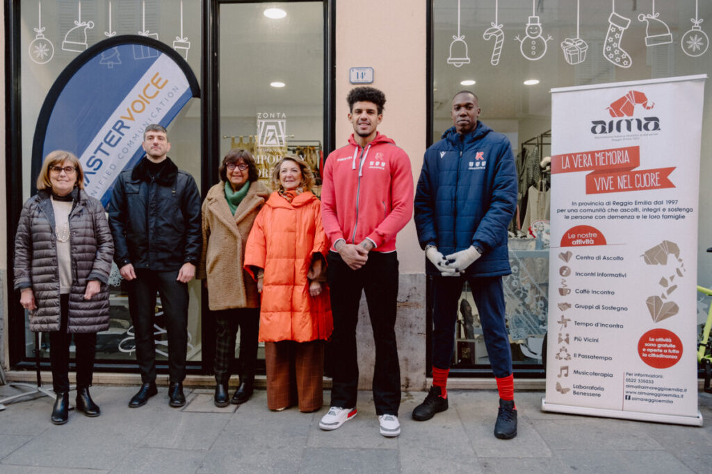 Michele Faedda di MasterVoice e Simonetta Cavalieri di AIMA insieme ai volontari di AIMA e Zonta e ai giocatori di Pallacanestro Reggiana  davanti al Temporary Store per il progetto We CaRE, il 19 dicembre 2024