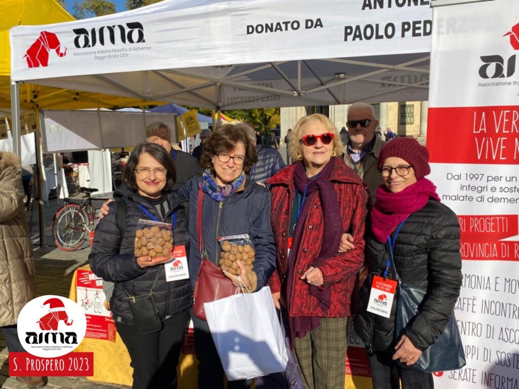Foto di gruppo: volontarie AIMA davanti allo stand con le Noci della Memoria in piazza Martiri nel giorno della Festa di San Prospero, 24 novembre 2023