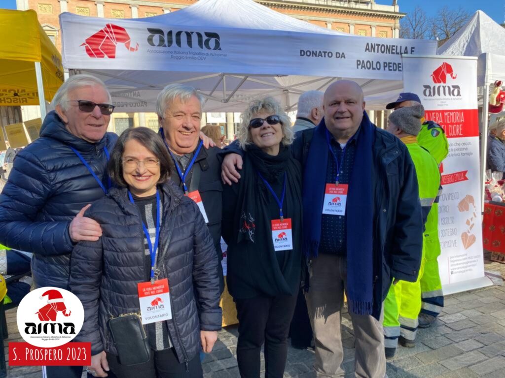 Foto di gruppo: volontarii AIMA davanti allo stand con le Noci della Memoria in piazza Martiri nel giorno della Festa di San Prospero, 24 novembre 2023