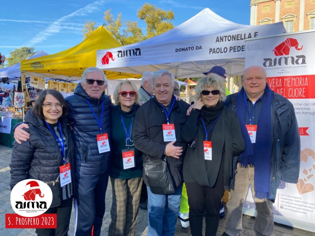 Foto di gruppo: volontarii AIMA davanti allo stand con le Noci della Memoria in piazza Martiri nel giorno della Festa di San Prospero, 24 novembre 2023